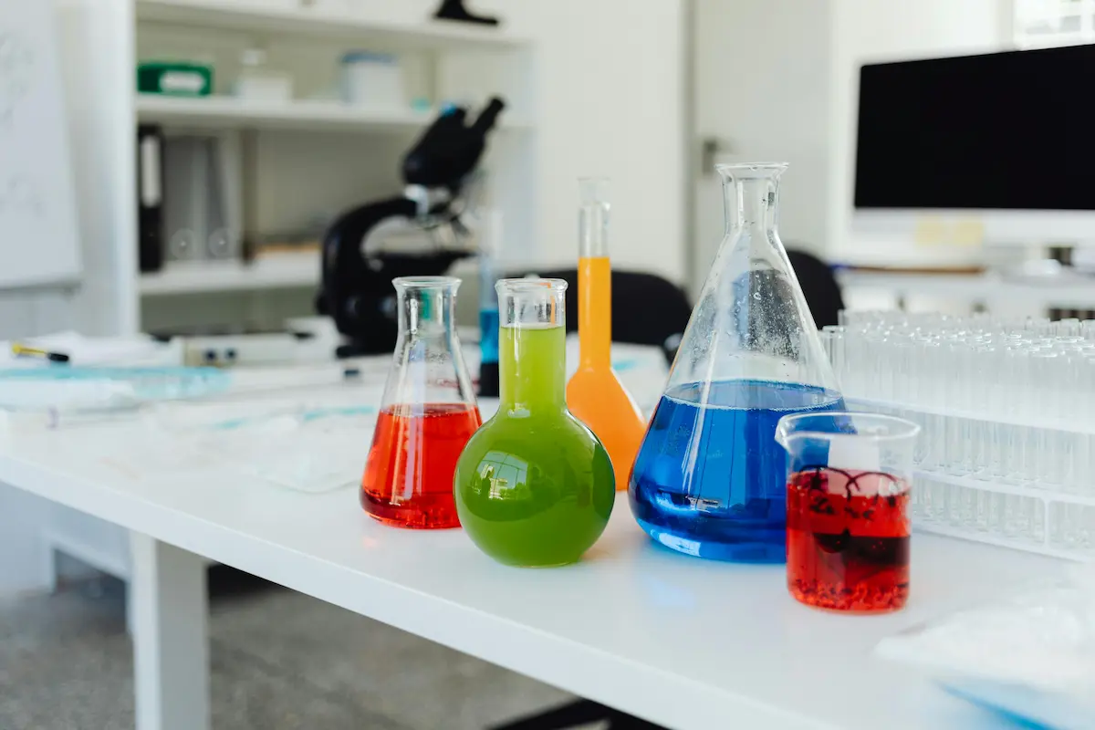 Laboratory table with various glass flasks and beakers containing colorful liquids in red, green, orange, and blue.